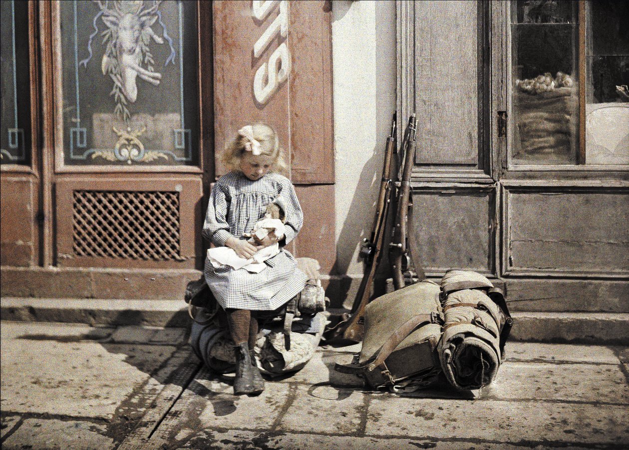 Mała dziewczynka bawiąca się lalką; obok niej na ziemi dwa pistolety i plecak, Reims, Marne, Francja, 1917 (autochrome) autorstwa Fernand Cuville