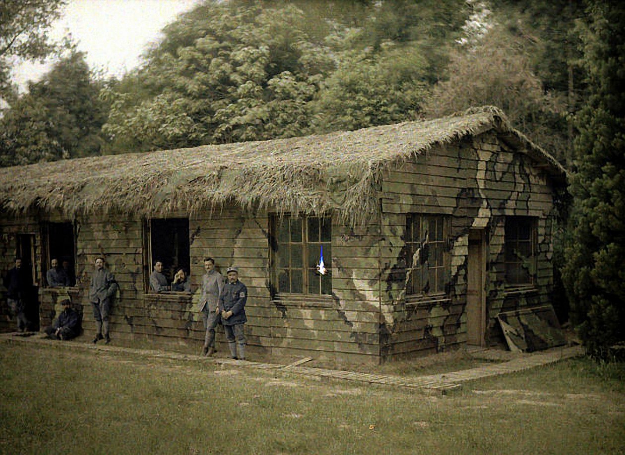 Dziewięciu francuskich żołnierzy przy drewnianym budynku w wojskowym kamuflażu, Soissons, Aisne, Francja, 1917 (autochrom) autorstwa Fernand Cuville